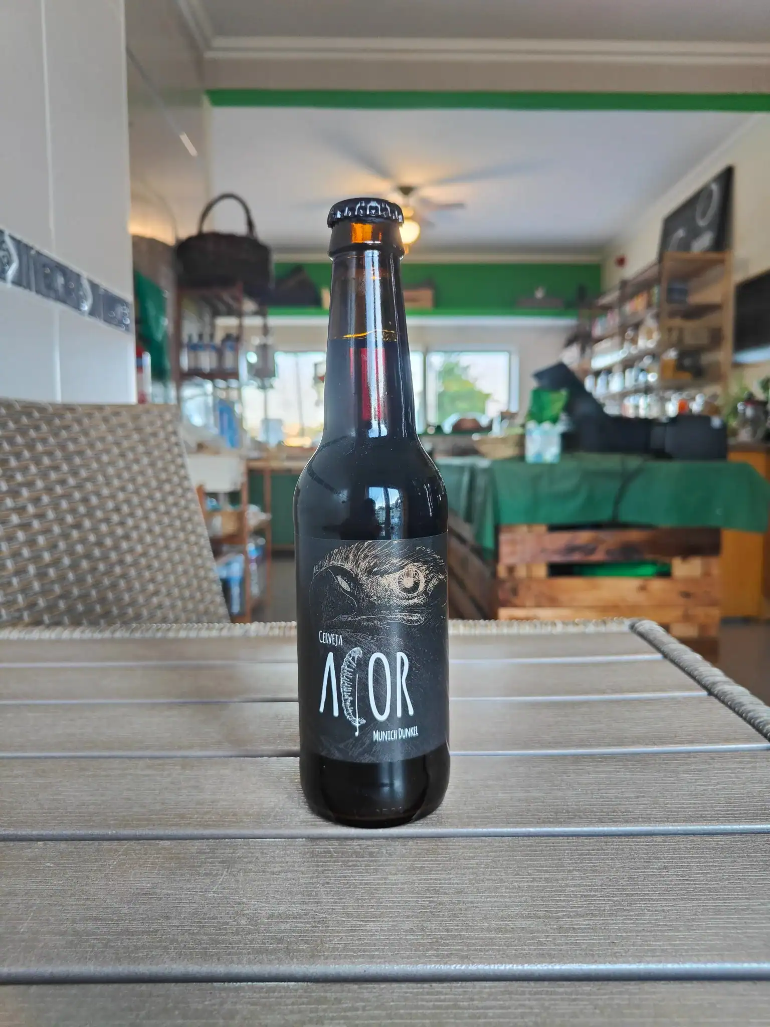 Cerveja artesanal escura com rótulo artístico em ambiente de loja de produtos frescos.